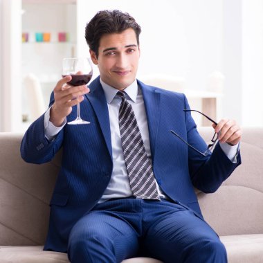 İş adamı evde oturmuş şarap içiyor.