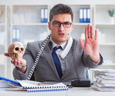 Ofisteki işadamı elinde insan kafatasıyla sigara içiyor.