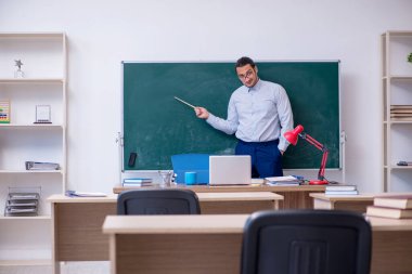 Genç erkek öğretmen yeşil panonun önünde.