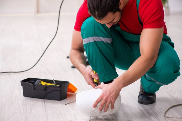 Young male contractor repairing fan heater indoors