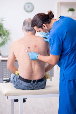 Yaşlı adam genç erkek doktor dermatoloğu ziyaret ediyor.