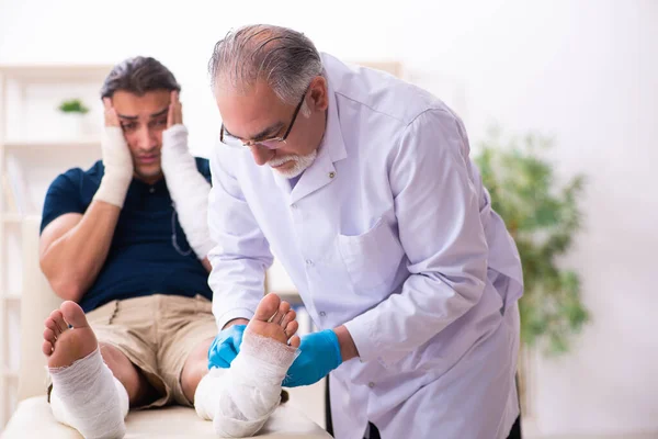 Ung skadad man besöker gammal läkare traumatolog — Stockfoto