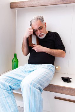 Yaşlı adam yatak odasında şarap içiyor.