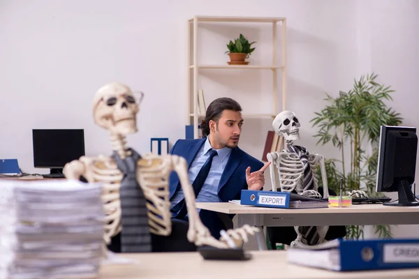 Junge männliche Angestellte mit Skeletten im Büro — Stockfoto