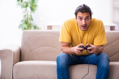 Genç adam evde joystick oynuyor.
