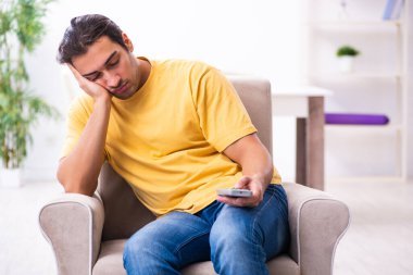 Genç adam evde televizyon izliyor.