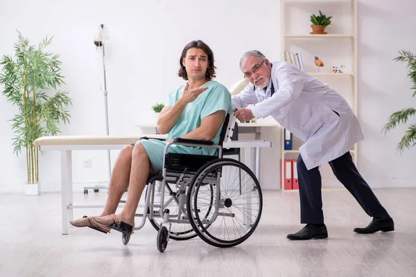 Jovem paciente do sexo masculino em cadeira de rodas e médico traumatologista experiente — Fotografia de Stock