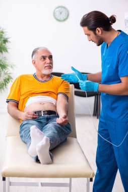 Yaşlı adam genç erkek doktoru ziyaret ediyor.