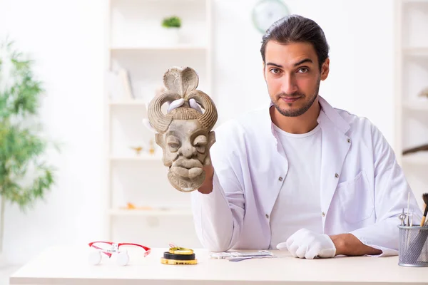 Joven arqueólogo masculino estudiando la antigua máscara de piedra africana — Foto de Stock