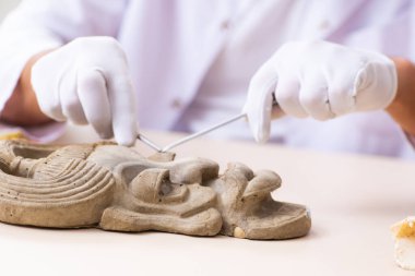 Genç erkek arkeolog eski Afrika taş maskesi üzerinde çalışıyor.