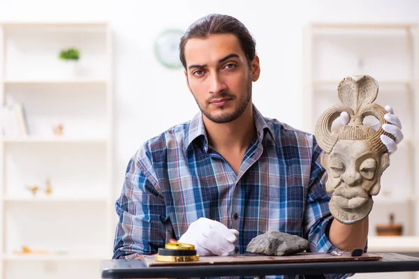 Joven arqueólogo masculino estudiando la antigua máscara de piedra africana —  Fotos de Stock