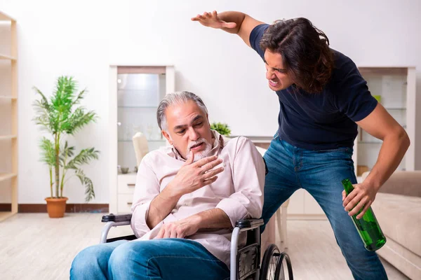 Oude man in rolstoel en jonge slechte verzorger binnen — Stockfoto