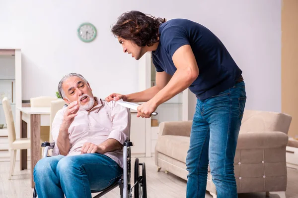 Vecchio in sedia a rotelle e giovane cattivo caregiver al chiuso — Foto Stock