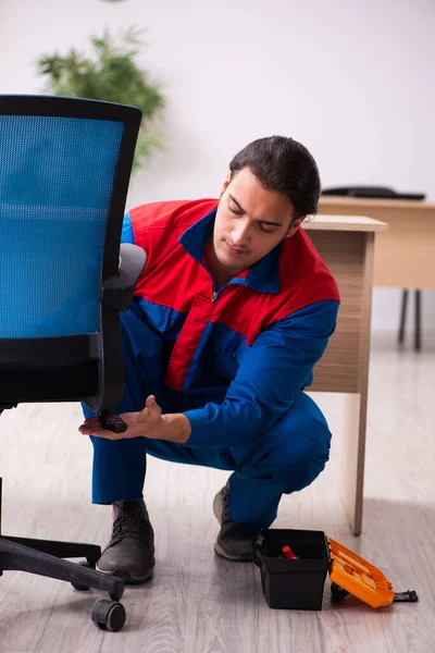 Jovem empreiteiro do sexo masculino reparando móveis no escritório — Fotografia de Stock