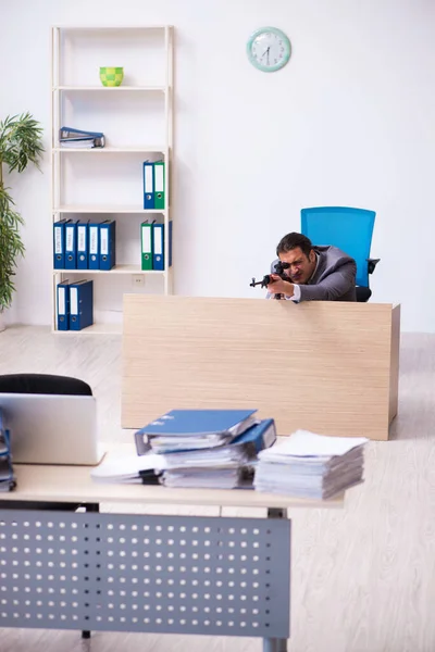 Young employee angry with excessive work holding firearm weapon — Stock Photo, Image