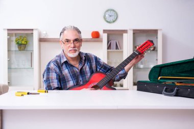 Yaşlı erkek tamirci evde müzik aletlerini tamir ediyor.