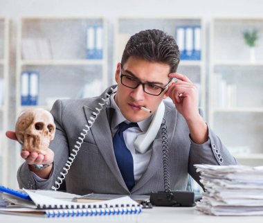 Ofisteki işadamı elinde insan kafatasıyla sigara içiyor.