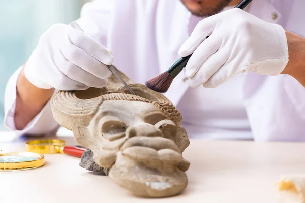 Jonge mannelijke archeoloog bestudeert het oude Afrikaanse steenmasker — Stockfoto