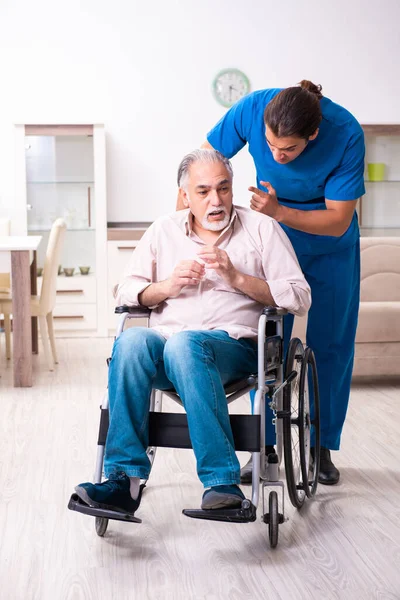 Oude man in rolstoel en jonge slechte verzorger binnen — Stockfoto