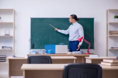 Genç erkek öğretmen yeşil panonun önünde.