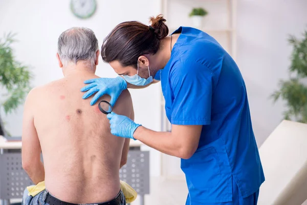 Homem velho visitando jovem médico dermatologista masculino — Fotografia de Stock