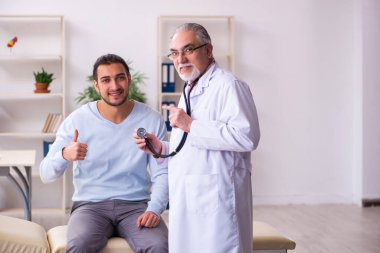 Genç hasta adam yaşlı doktoru ziyaret ediyor.