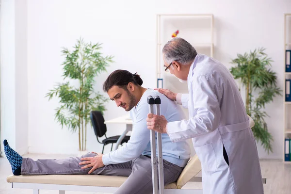 Young leg injured man visiting old doctor osteopath — Stock Photo, Image