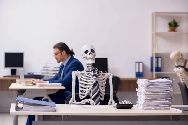 Fiatal férfi alkalmazott csontvázakkal az irodában — Stock Fotó