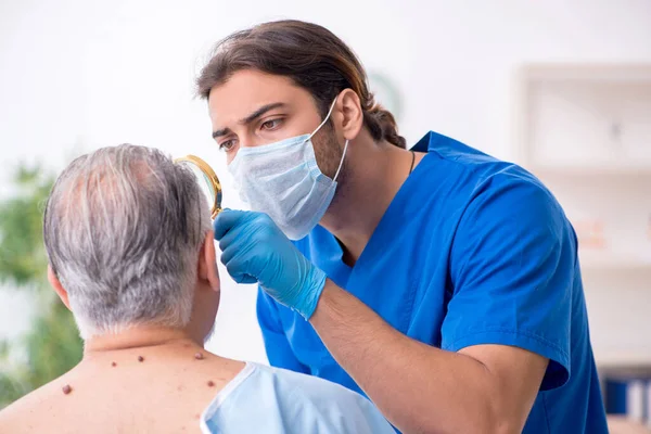 Homem velho visitando jovem médico dermatologista masculino — Fotografia de Stock