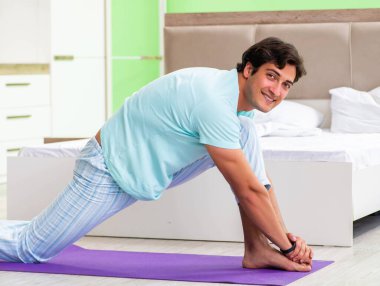 Pijamalı genç adam sabah egzersizi yapıyor.