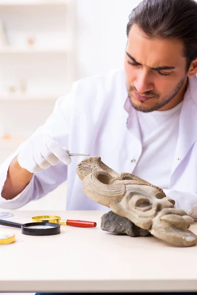Jonge mannelijke archeoloog bestudeert het oude Afrikaanse steenmasker — Stockfoto