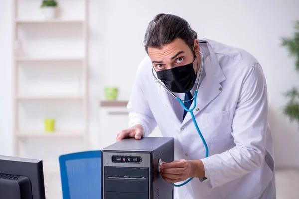 Joven doctor masculino con estetoscopio reparando computadora —  Fotos de Stock