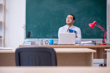 Genç erkek öğretmen yeşil panonun önünde.