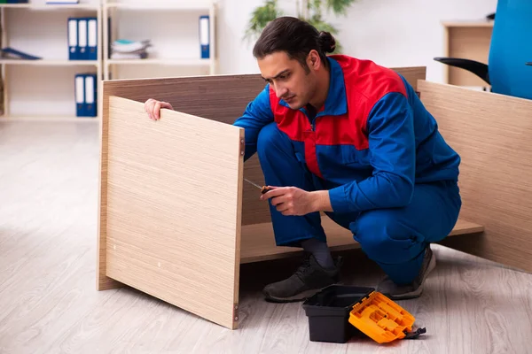 Young male contractor repairing furniture in the office