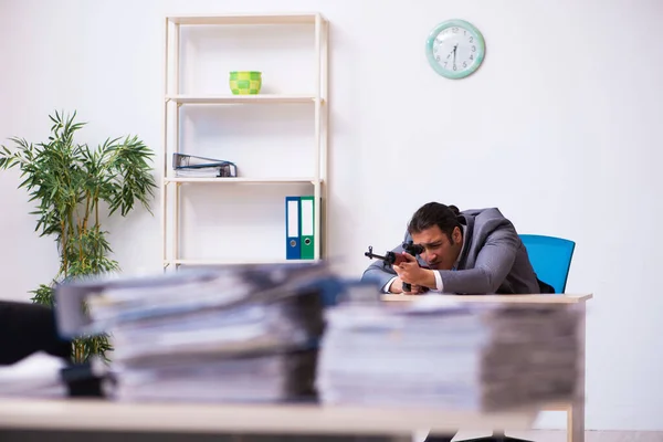 Young employee angry with excessive work holding firearm weapon — Stock Photo, Image