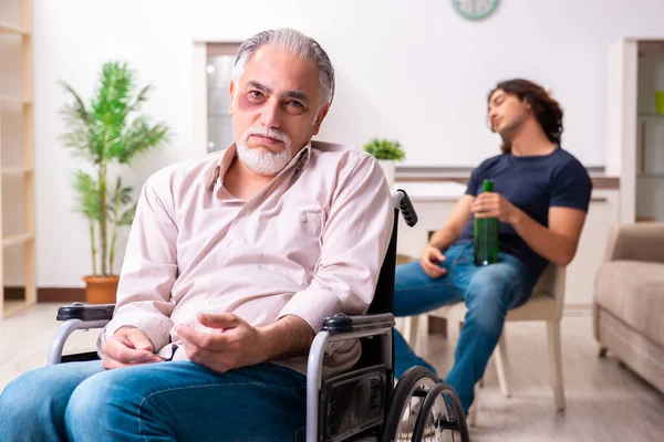 坐在轮椅上的老人和在室内的糟糕的年轻照顾者 — 图库照片
