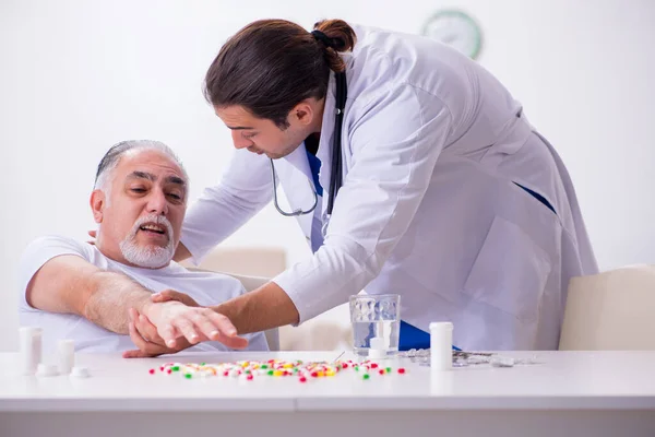 Joven médico masculino visitando a viejo paciente masculino en casa —  Fotos de Stock