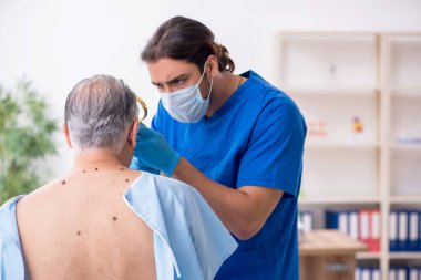 Yaşlı adam genç erkek doktor dermatoloğu ziyaret ediyor.