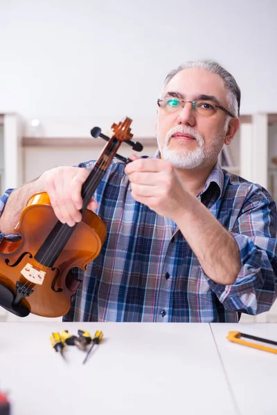 Senior mannelijke reparateur die thuis muziekinstrumenten repareert — Stockfoto
