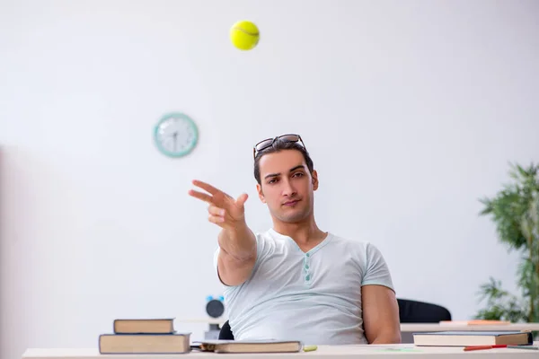 Joven estudiante masculino lanzando pelota de tenis durante la preparación del examen — Foto de Stock