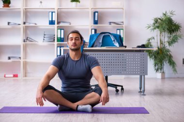 Genç yakışıklı çalışan ofiste spor egzersizleri yapıyor.