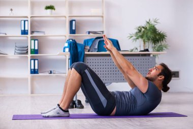 Genç yakışıklı çalışan ofiste spor egzersizleri yapıyor.