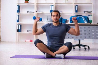 Genç yakışıklı çalışan ofiste spor egzersizleri yapıyor.