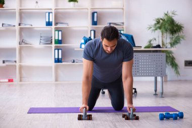 Genç yakışıklı çalışan ofiste spor egzersizleri yapıyor.