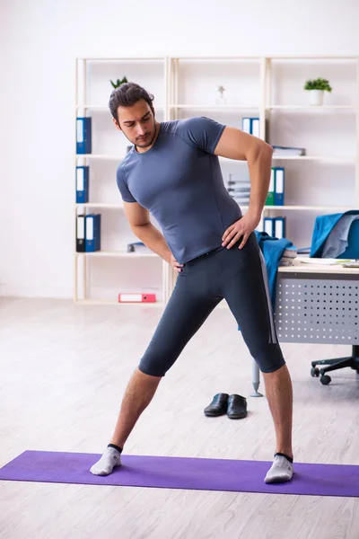 Young handsome employee doing sport exercises in the office — Stock Photo, Image