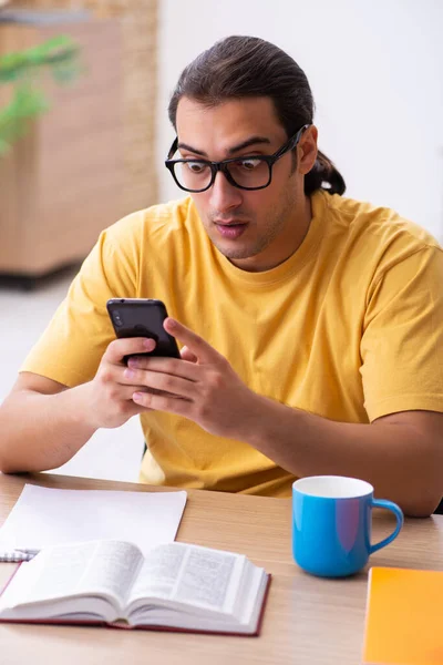 Ung manlig student som håller mobiltelefon under tentamen förberedelse — Stockfoto