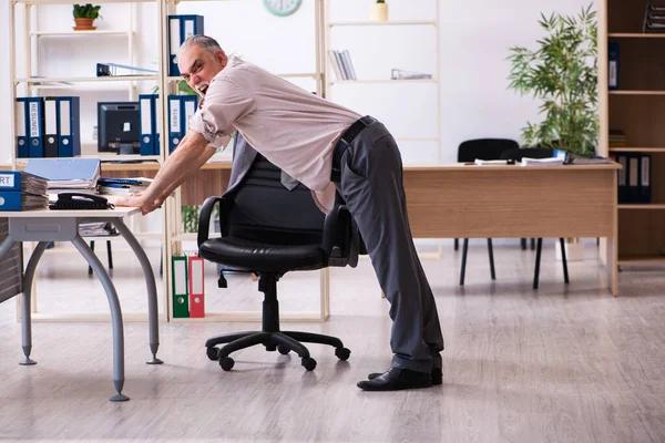 Velho funcionário do sexo masculino fazendo exercícios físicos no local de trabalho — Fotografia de Stock