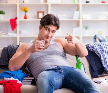 Dağınık bir odada alkol alan genç bir öğrenci.