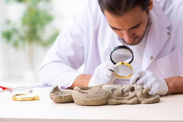 Jonge mannelijke archeoloog bestudeert het oude Afrikaanse steenmasker — Stockfoto