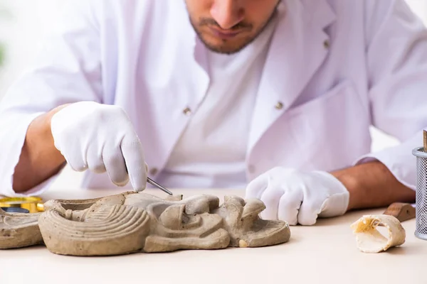 Jonge mannelijke archeoloog bestudeert het oude Afrikaanse steenmasker — Stockfoto